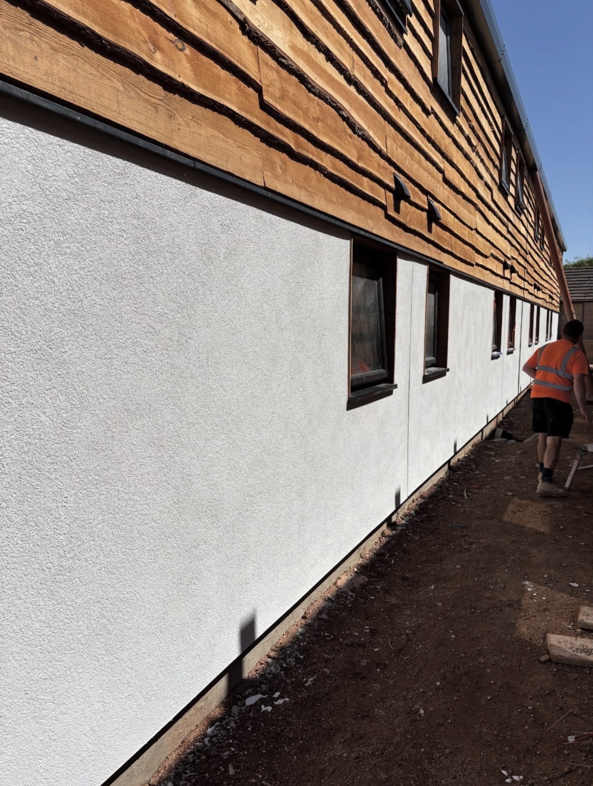 Long external wall finished in white silicone render alongside timber cladding